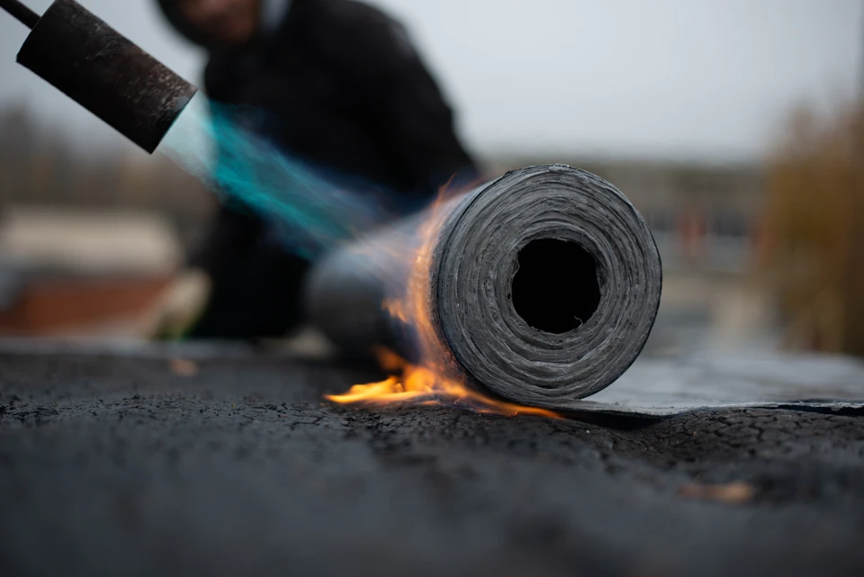 Gros plan sur une toiture en tuiles ou plaques ondulées de qualité, impeccablement posée et étanche, photographiée sous angle légèrement plongeant par temps nuageux ou après pluie, avec quelques gouttes d'eau ruisselant efficacement sur la surface. La toiture doit apparaître robuste, bien entretenue et professionnelle, illustrant la protection fiable apportée par une imperméabilisation réussie.